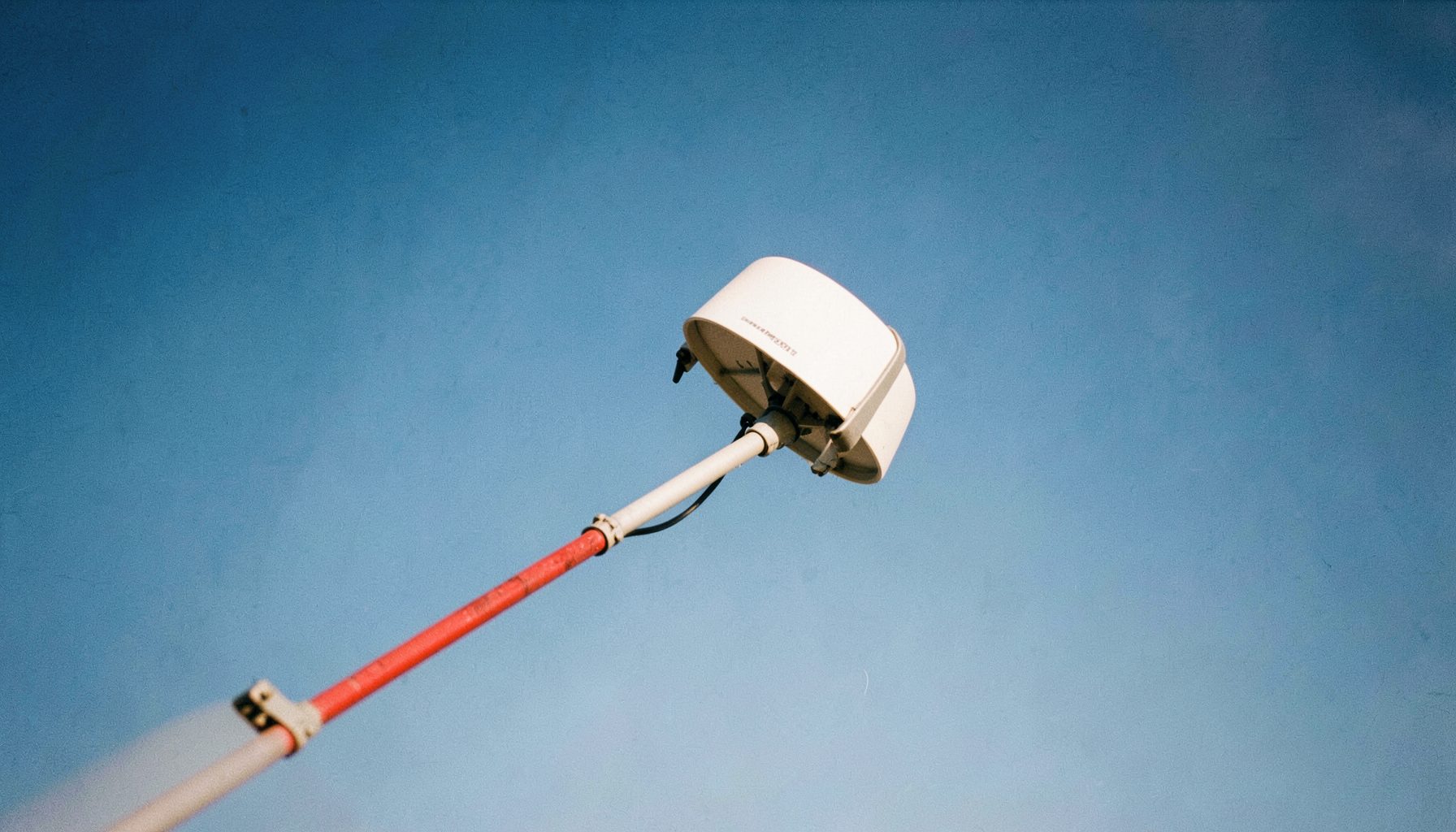 Parabole blanche sur fond de ciel bleu dégagé, orientée vers le sud, avec un LNB visible au bout du bras de fixation.