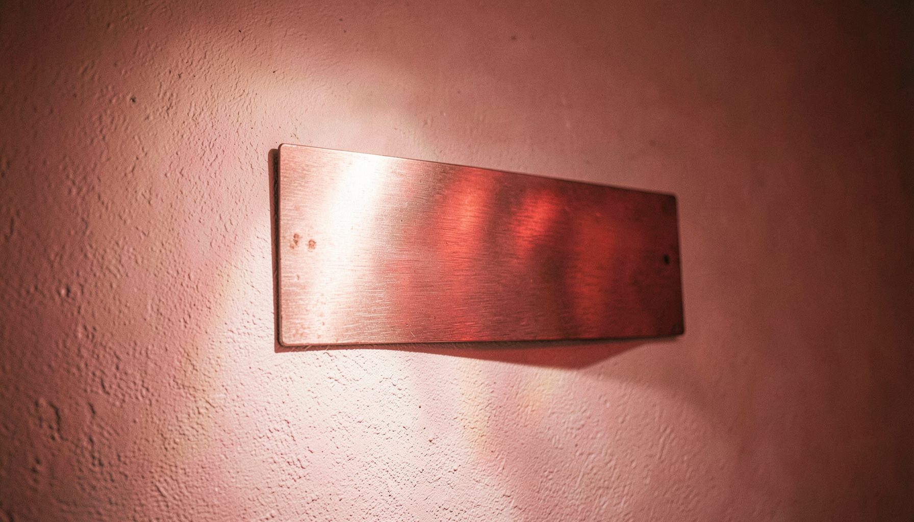 Applique murale design en métal brossé projetant une lumière douce sur un mur blanc texturé