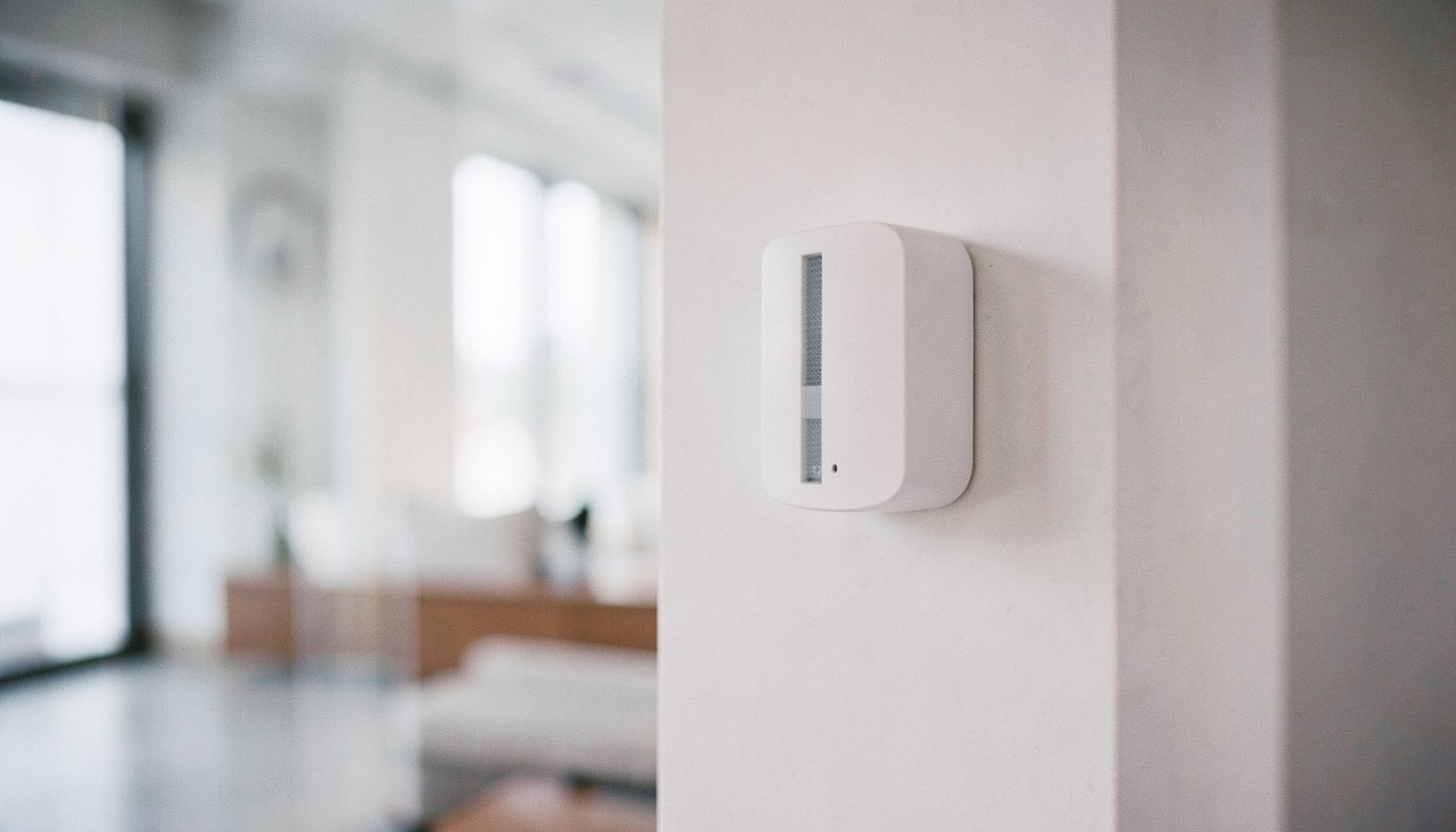 Détecteur de mouvement blanc fixé au mur, arrière-plan flou de pièce contemporaine, tons blancs et gris clair