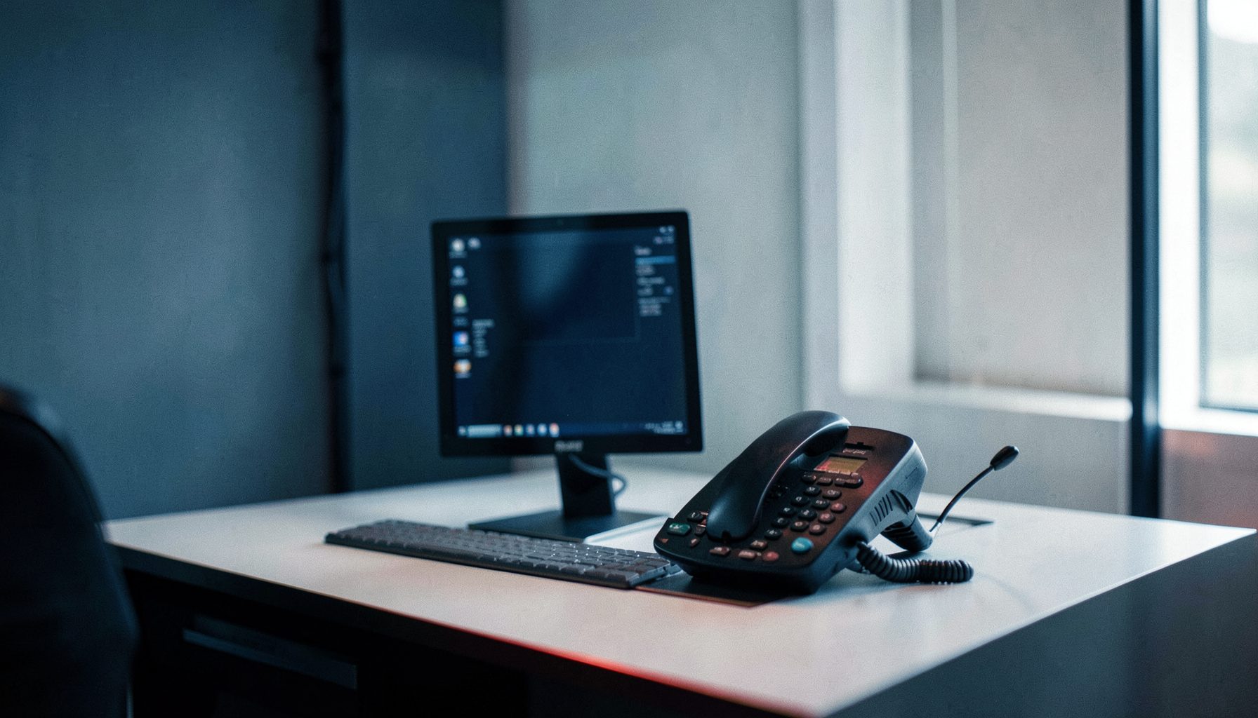 Bureau moderne avec écran et téléphone, ambiance calme aux tons bleu marine et gris clair, lumière douce tamisée