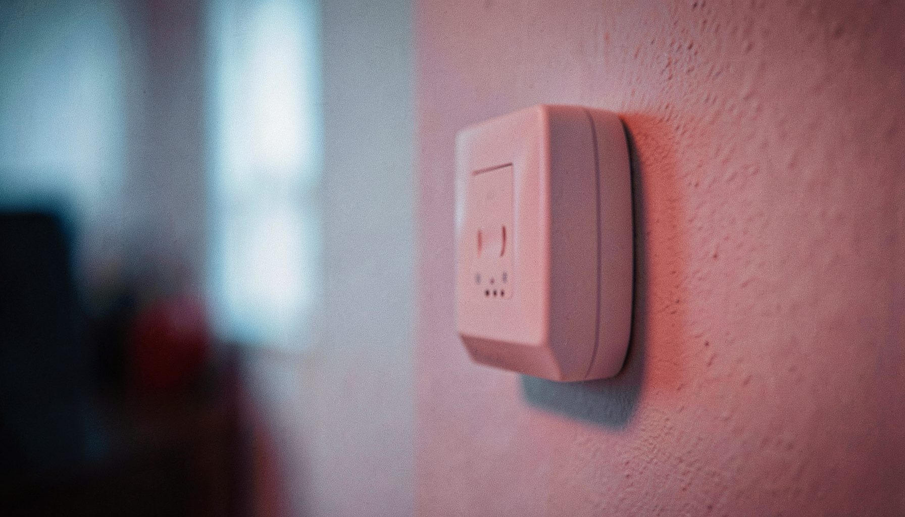 Détail flou d'un petit boîtier domotique blanc fixé au mur, lumière douce bleutée en arrière-plan